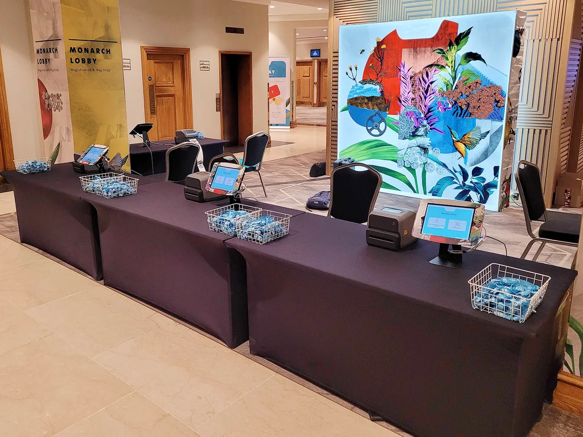 A self check-in station in an event lobby: check-in tablets and badge printers set up for attendees to badge themselves in.